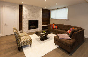 Newly renovated basement with ceiling lights and light brown wood floors and furniture and white stone fireplace and rug