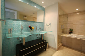 Picture of blue glass walls and sink bathroom. Tan marble shower, tub and flooring with backlighting on large mirron on the wall.