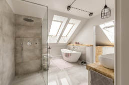 Gray and white bathroom picture with modern tub and stand up shower. Gray marble flooring with rustic black iron lighting. Two large roof angled skylights brighten the room.