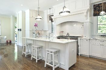 Kitchen with white cabines, walls, stools and gray marbled countertops. Stainless steel appliances and pendant lighting. Rustic wood floors. A mix of french and traditional style of kitchen.