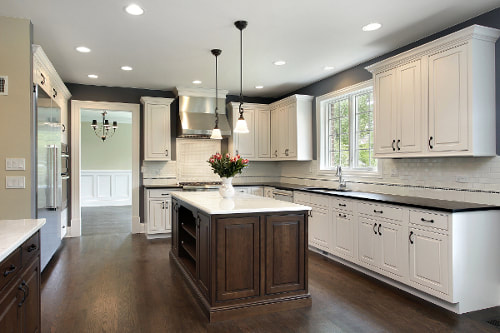 Picture of kithen with dark wood floors and island. White marble island countertop and cabinets. Black marble countertops on top of cabinets that run around the exterior of kitchen. Recessed lighting with black and white pendants. White subway tile backsplash.